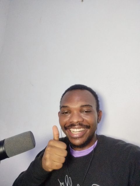 Wisdom Okonkwo smiling while recording beside his podcast microphone